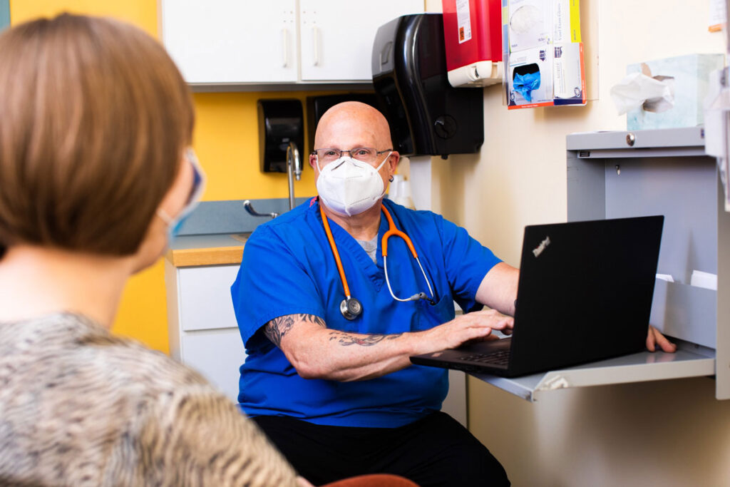Doctor talking to patient while taking notes on laptop